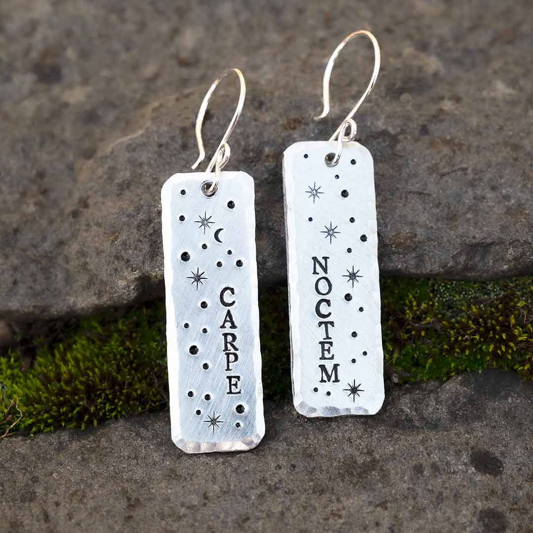Earrings hand-stamped with the words "carpe noctem" and stars, resting against a background of stone and moss. Excellent science jewelry gift for stargazers, astronomers, and night lovers.