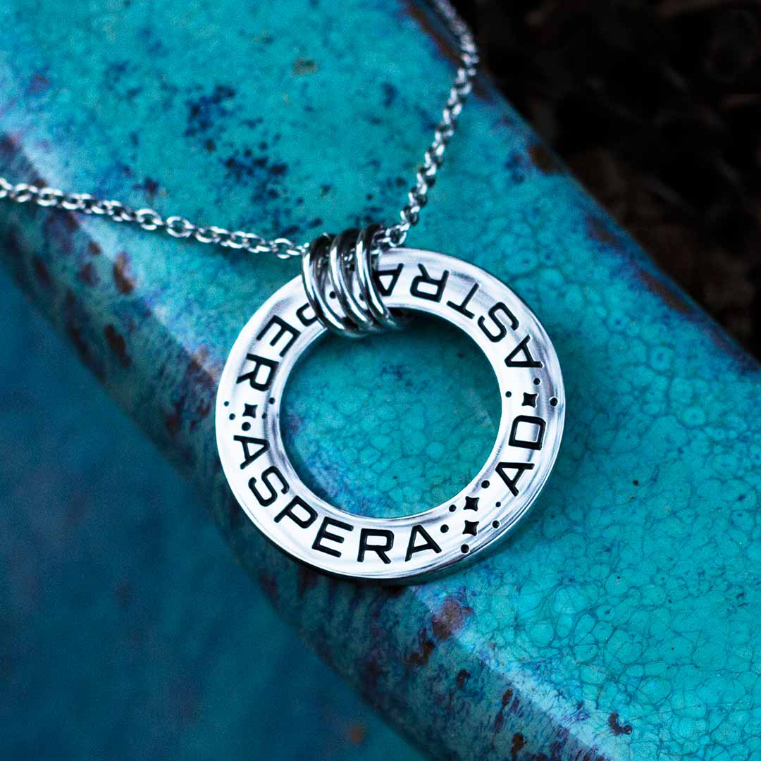 Ad Astra Per Aspera Necklace - Perfect science jewelry gift for space science enthusiasts, astronomy students &amp; instructors, and anyone with a dream to follow, despite the challenges. Steel disc pendant is engraved with the Latin phrase “AD ASTRA PER ASPERA”, which translates as “to the stars, through difficulties”. Each word is framed with tiny stars, and the pendant freely moves within three steel jump rings and is hung on an adjustable 16-18 inch steel chain.
