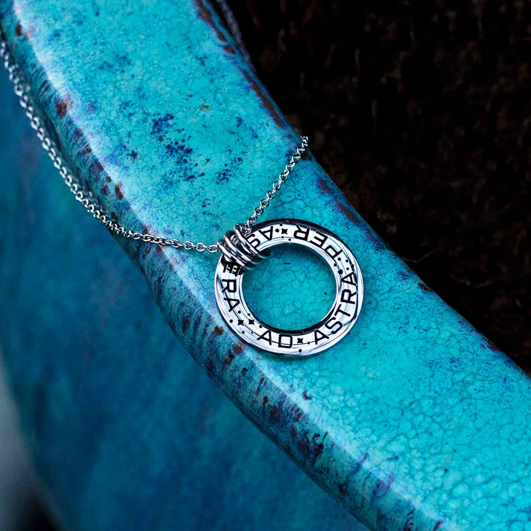 Ad Astra Per Aspera Necklace - Perfect science jewelry gift for space science enthusiasts, astronomy students &amp; instructors, and anyone with a dream to follow, despite the challenges. Steel disc pendant is engraved with the Latin phrase “AD ASTRA PER ASPERA”, which translates as “to the stars, through difficulties”. Each word is framed with tiny stars, and the pendant freely moves within three steel jump rings and is hung on an adjustable 16-18 inch steel chain.