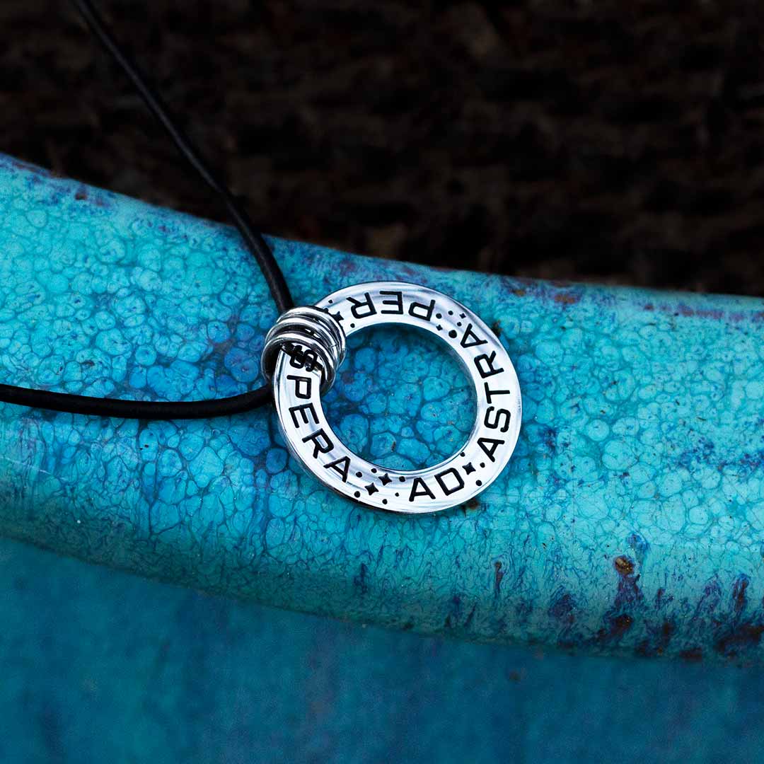 Ad Astra Per Aspera Necklace - Perfect science jewelry gift for space science enthusiasts, astronomy students &amp; instructors, and anyone with a dream to follow, despite the challenges. Steel disc pendant is engraved with the Latin phrase “AD ASTRA PER ASPERA”, which translates as “to the stars, through difficulties”. Each word is framed with tiny stars, and the pendant freely moves within three steel jump rings and is hung on an adjustable black leather cord.