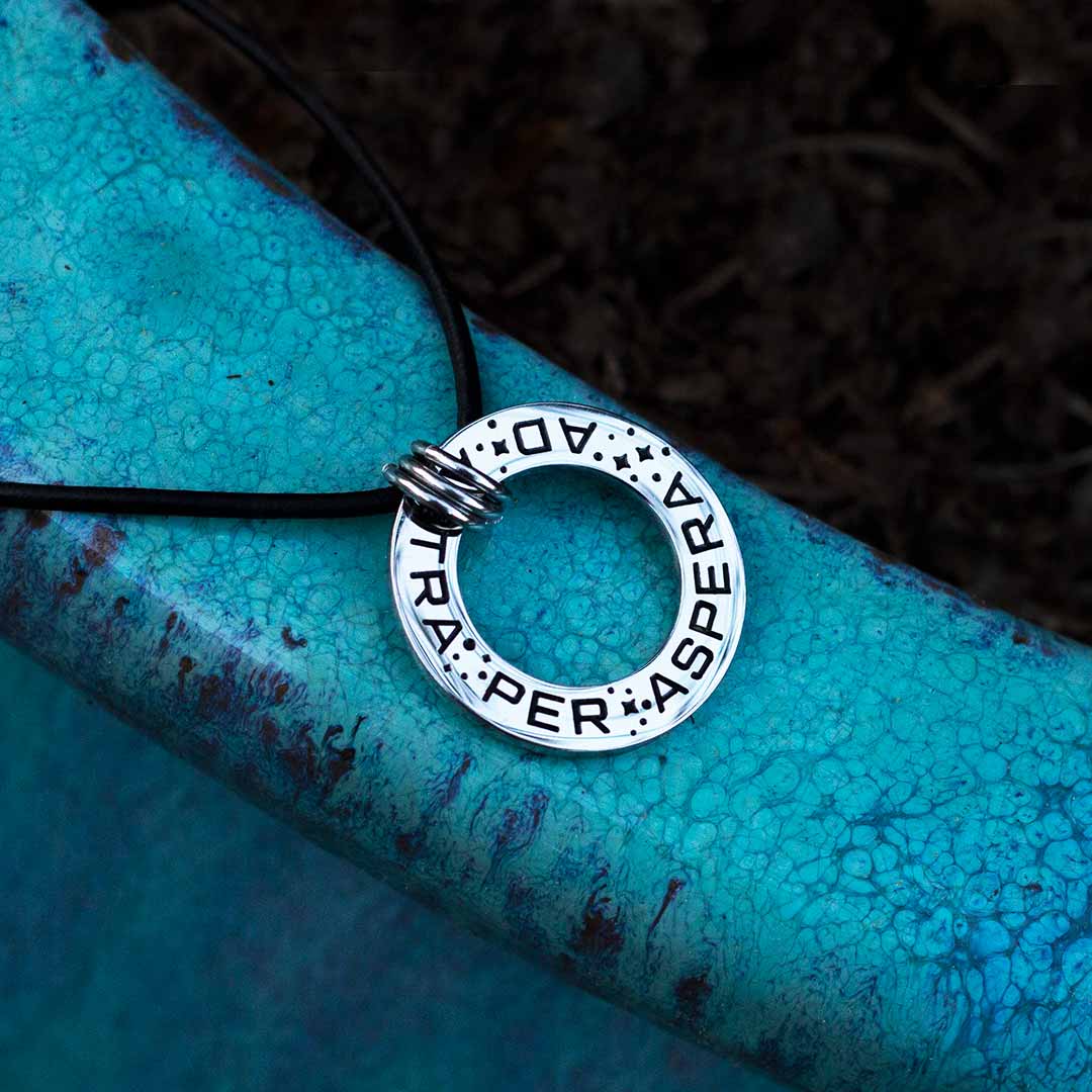 Ad Astra Per Aspera Necklace - Perfect science jewelry gift for space science enthusiasts, astronomy students &amp; instructors, and anyone with a dream to follow, despite the challenges. Steel disc pendant is engraved with the Latin phrase “AD ASTRA PER ASPERA”, which translates as “to the stars, through difficulties”. Each word is framed with tiny stars, and the pendant freely moves within three steel jump rings and is hung on an adjustable black leather cord.