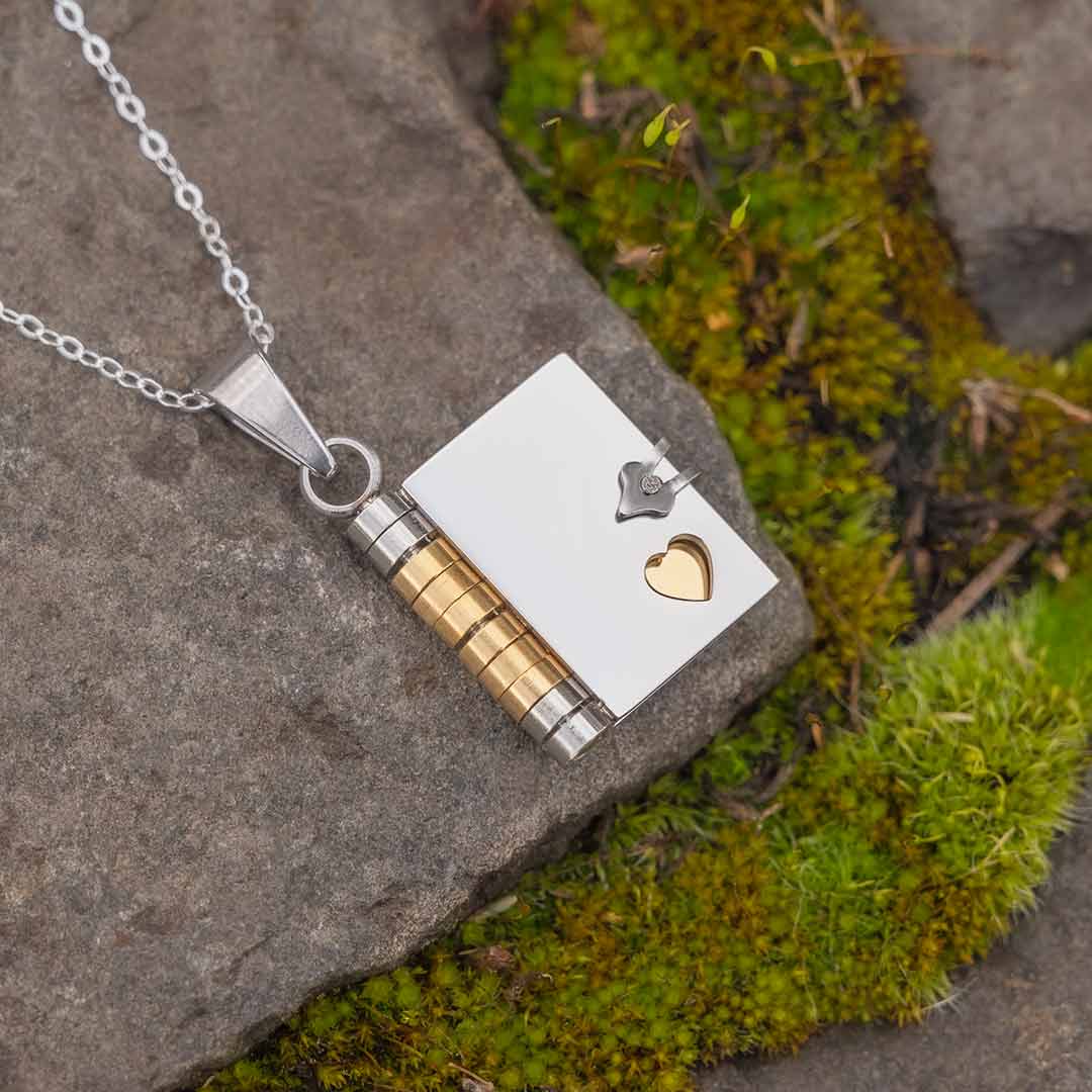 Book Necklace - jewelry gift for a writer, librarian, teacher, historian, or book lover. Photo of book pendant on a stone background, with green moss surrounding it.