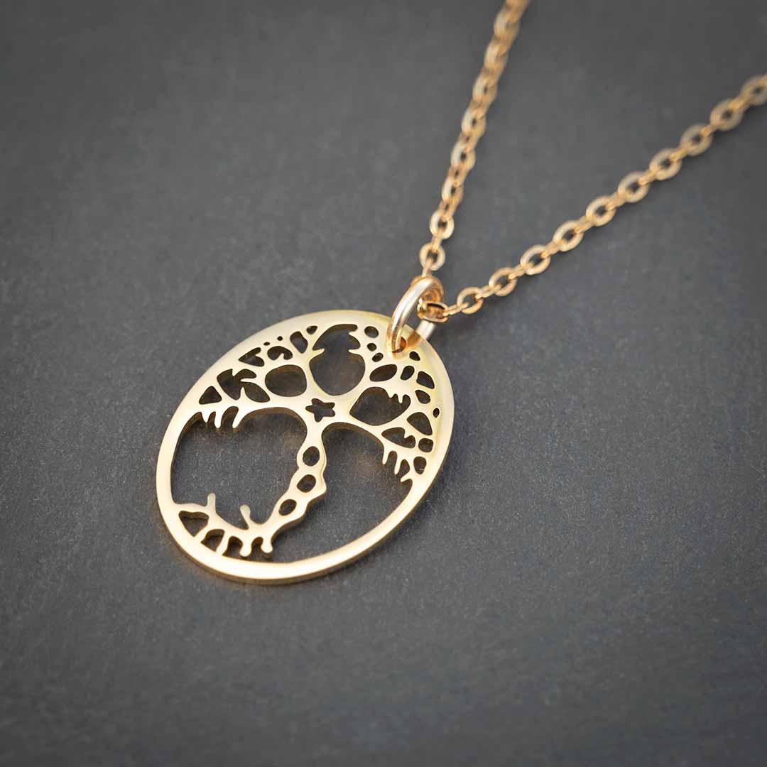 Angled photo of gold plated steel pyramidal neuron pendant with a gold chain, resting on a grey rock.